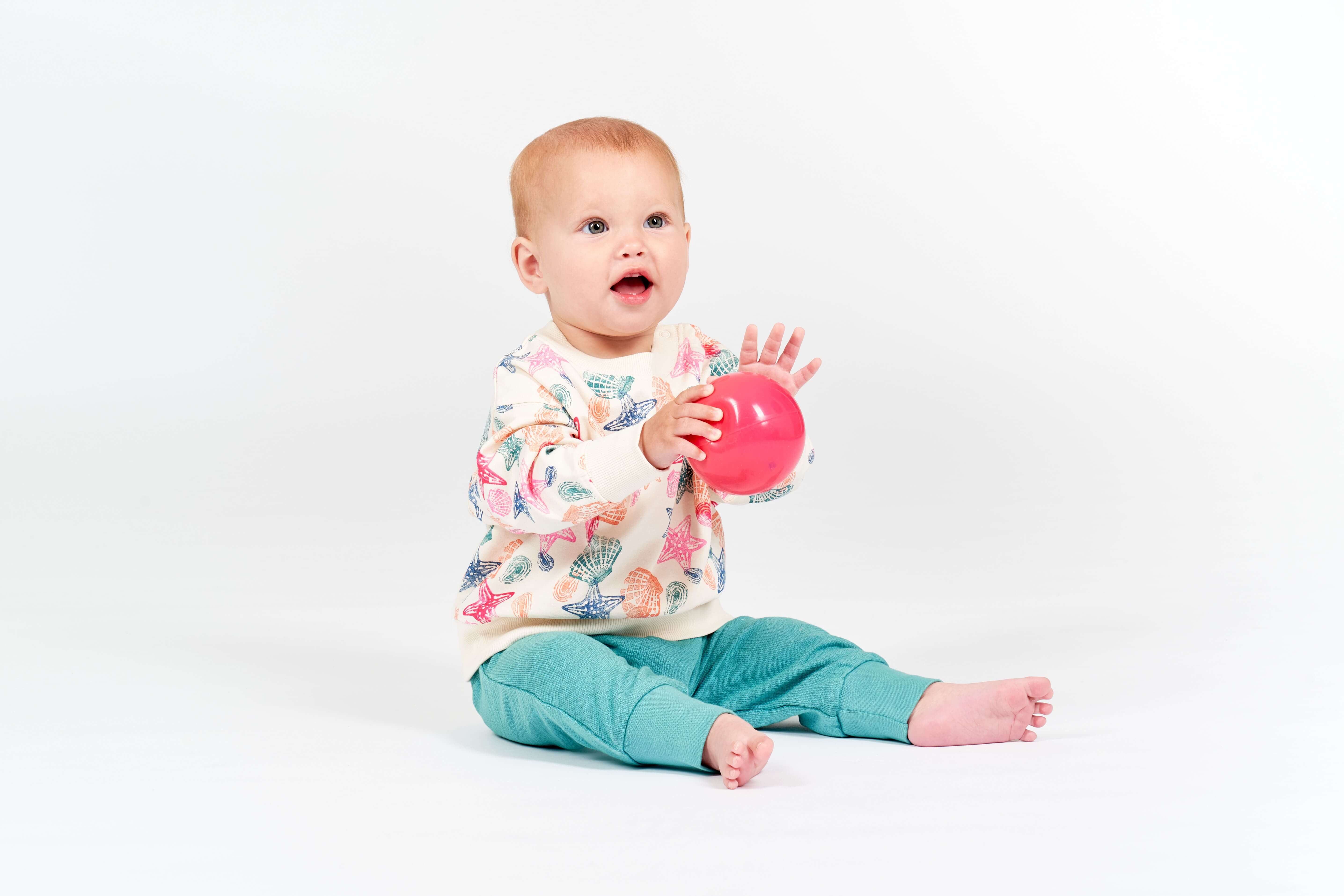 Baby mit coolem Outfit hält Ball in der Hand